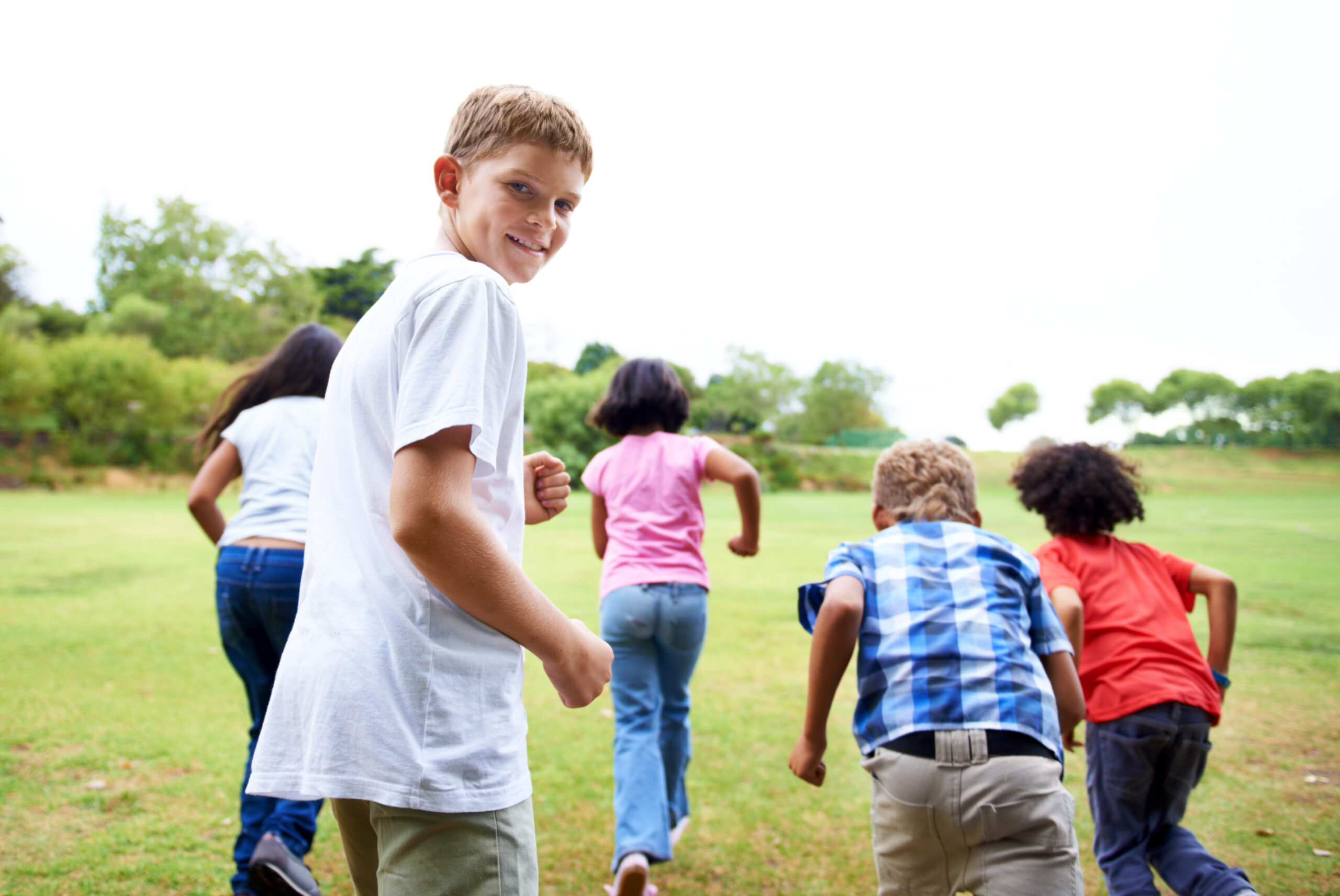 One child looking back at the camera smiling and several others running away across a field.